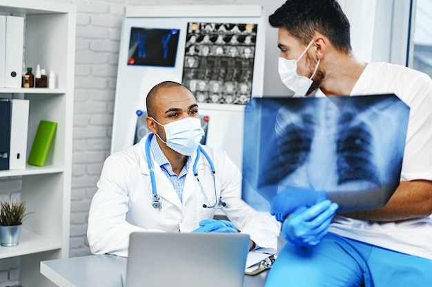 Two male doctors examine an x-ray of lungs in hospital cabinet