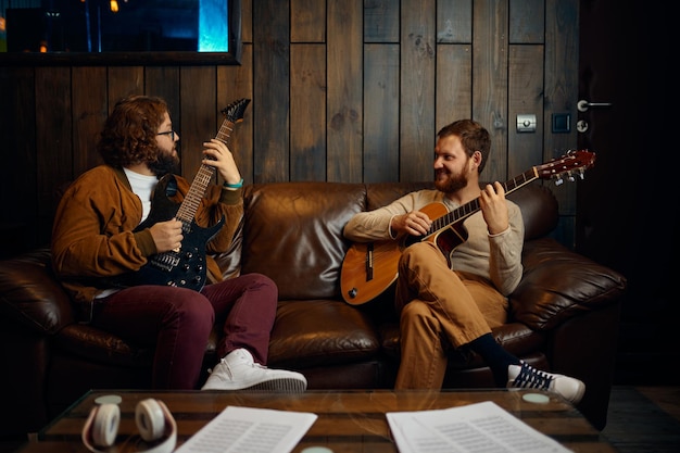 Two male friends playing guitar at home together. Musicians enjoy hobby activity at home studio