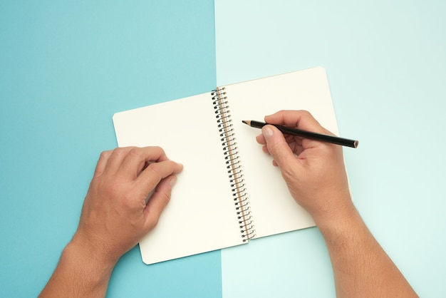 Two male hands holding open notepad with empty white sheets, top view