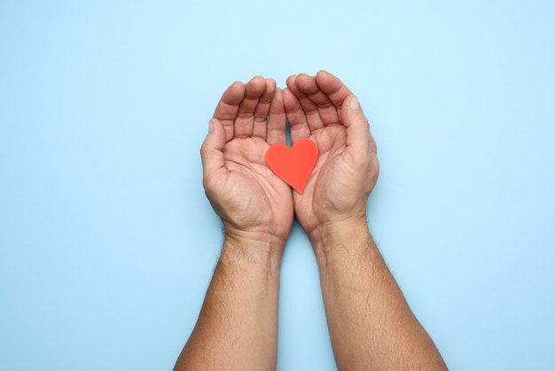 Due mani maschii che lottano cuore di carta rosso su un blu