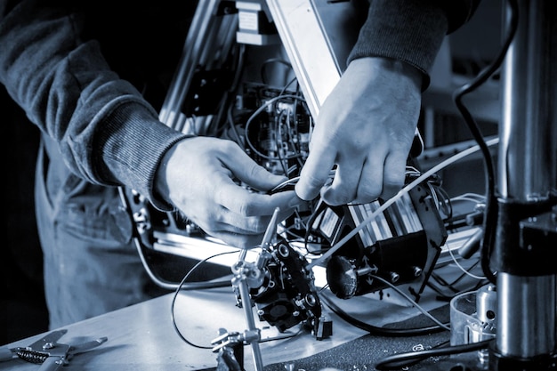 Два мастера-мужчины работают в мастерской с электроникой, проводами, 3D-принтером.