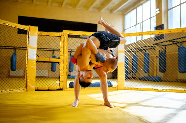 Two male MMA fighters fights in a cage in gym.