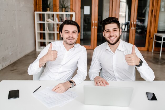 Two male office workers show thumbs up in the office