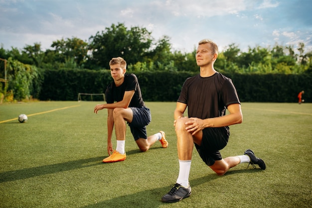 Two male soccer players doing stretching exercise on the field. Football training on outdoor stadium, workout before game