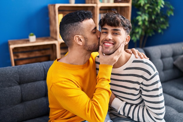 Two man couple hugging each other and kissing sitting on sofa at home