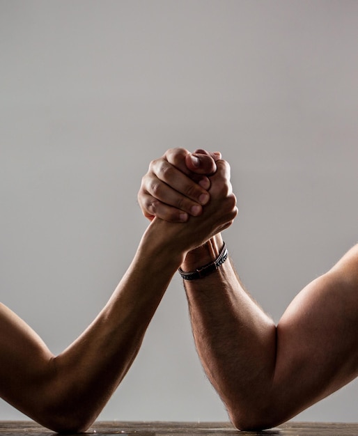 Two man's hands clasped arm wrestling strong and weak unequal match Heavily muscled man arm wrestling a puny weak man