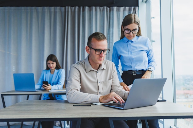 Two manager employees in a modern office Europeans man and woman working at a table with a laptop colleagues discuss and consult think about a joint project