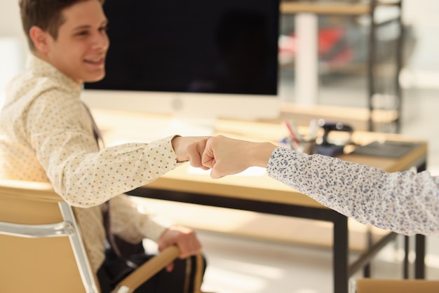 Photo two managers touching each other by fists while sitting at their office desks symbol of consent