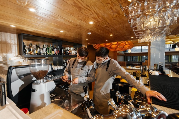 Two masked baristas prepare exquisite delicious coffee at the bar in the coffee shop The work of restaurants and cafes during the pandemic