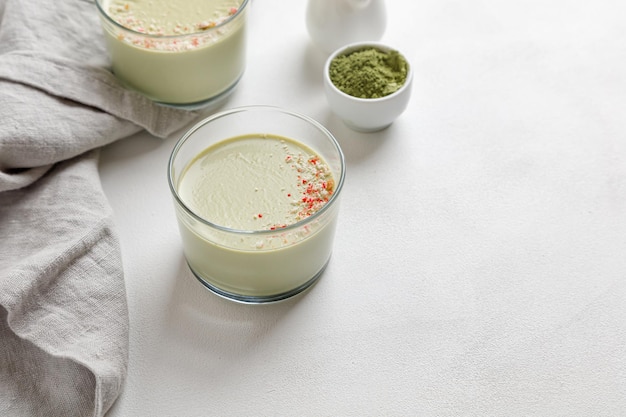 Two matcha tea panna cotta desserts with decor in a glass on a white background and a grey napkin