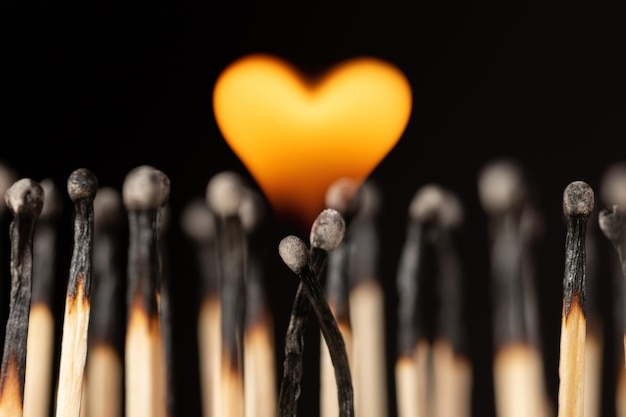 Two matches hanging each other and burning with flame in shape of a heart. Concept of love