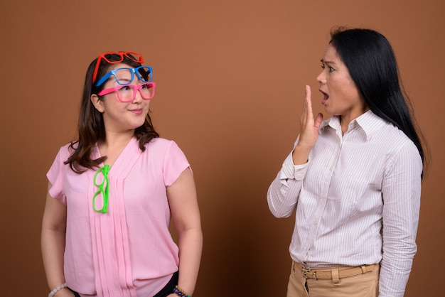 Two mature Asian businesswomen together against brown wall