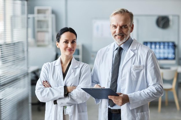 Two mature successful general practitioners in lab coats looking at camera