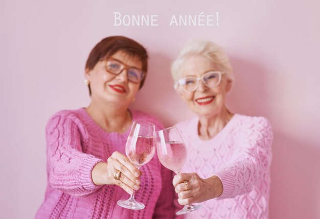 Photo two mature women in pink sweaters drinking wine and celebrating