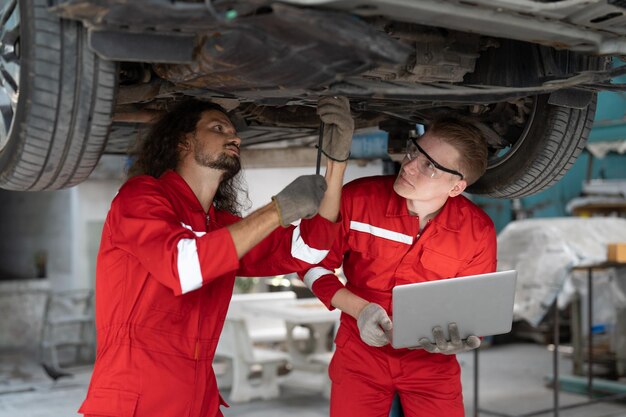 Photo two mechanic man repairing axle and suspension under car