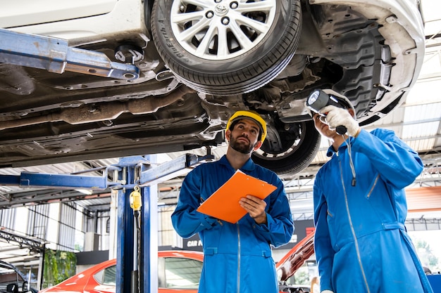 Two mechanic was checking the car suspension. Vehicle raised on lift at maintenance station. Car mechanic working at automotive service center.