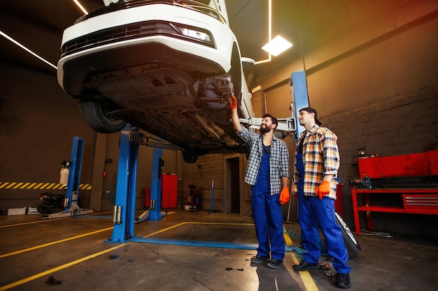 Two mechanics checking car suspension in repairing workshop