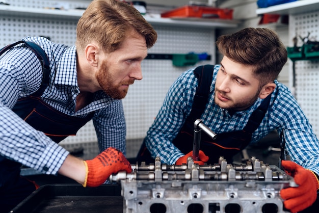 Two mechanics stand and look at the part with a breakdown.