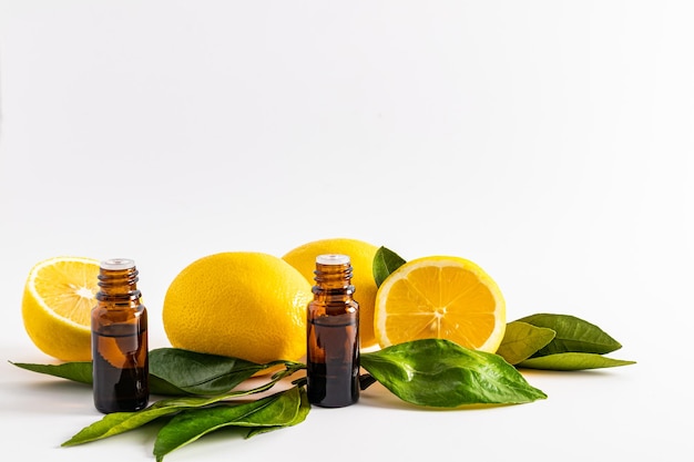 Two medical bottles of dark glass with a dropper with lemon essential oil on a white background among ripe fruits and leaves aromatherapy