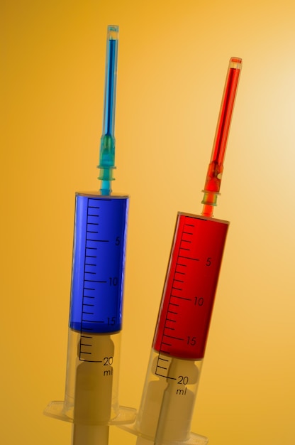 Two medical syringes one with the vaccine and one with the test blood on yellow background