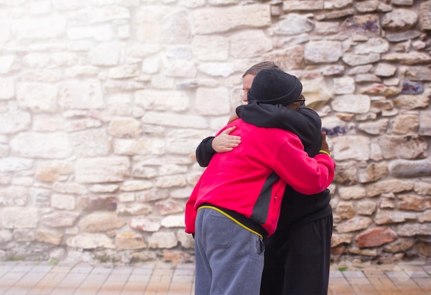 Two men an AfricanAmerican and a European embrace when meeting at a stone wall