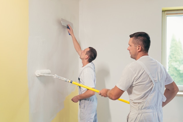 Two men apply plaster to the wall and repair the house