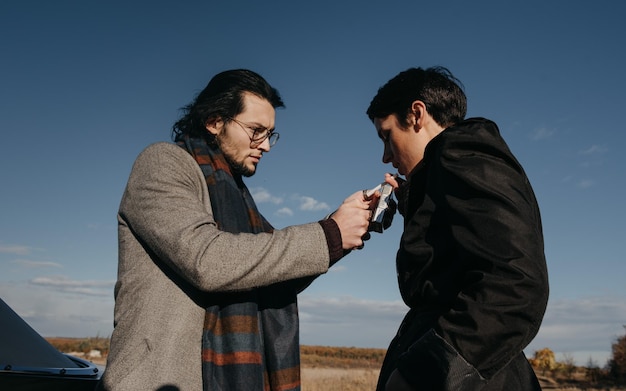 Two men are lighting a cigarette in a field.