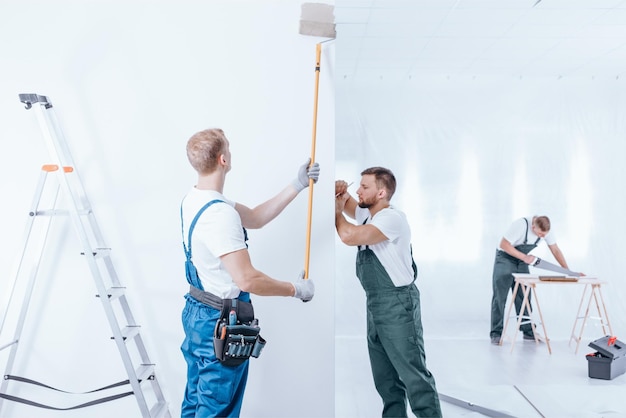 Two men are painting a wall with a paint roller.