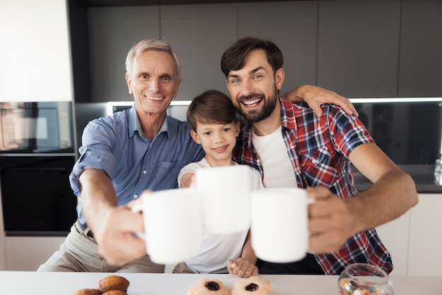 Two men and a boy are posing in the kitchen with cups