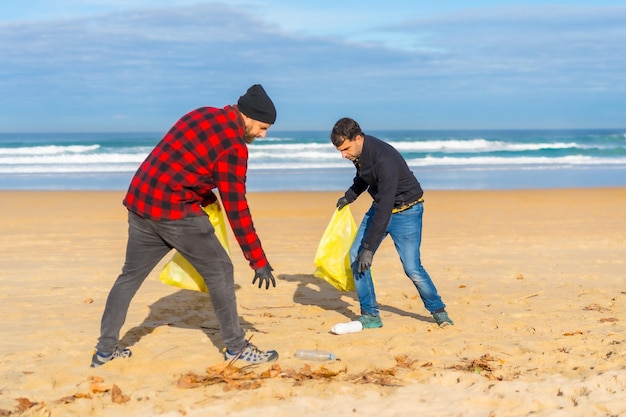 Photo two men collecting plastic on the beach ecology concept sea pollution