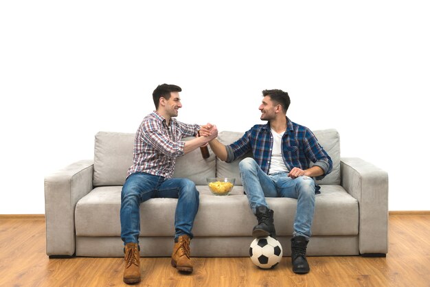 I due uomini bevono una birra sul divano sullo sfondo bianco