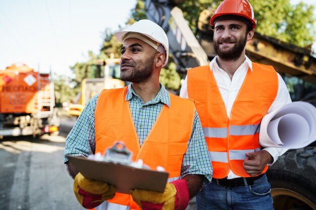 Due ingegneri discutono del loro lavoro in piedi contro le macchine edili