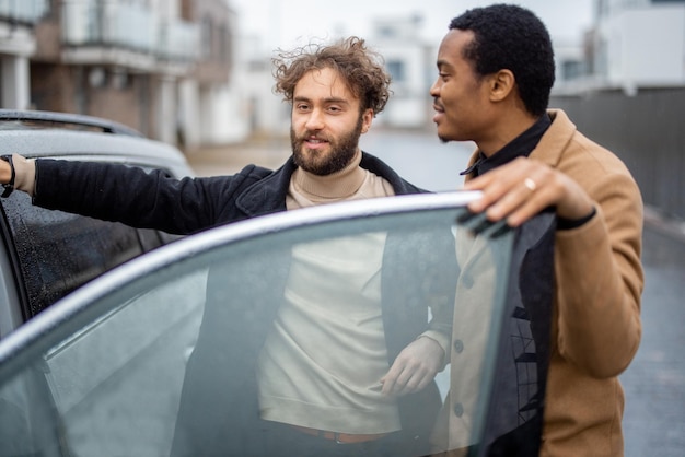 Двое мужчин флиртуют, стоя возле машины на улице