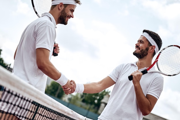 2人の男性プロテニスプレーヤーがテニスの試合の前後に握手します