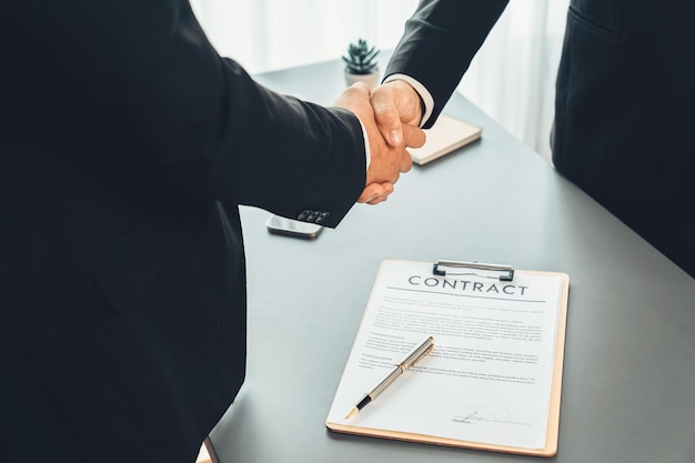 Two men shaking hands over a contract on a desk