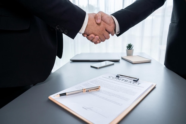 Two men shaking hands over a contract on a desk