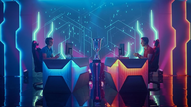 Two men sit behind a podium with a blue and red sign that says esports on it.