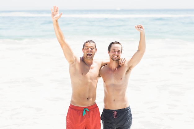 Two men standing beach with hands raised