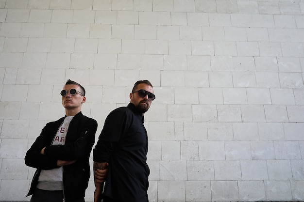 Two men in sunglasses against a brick wall background