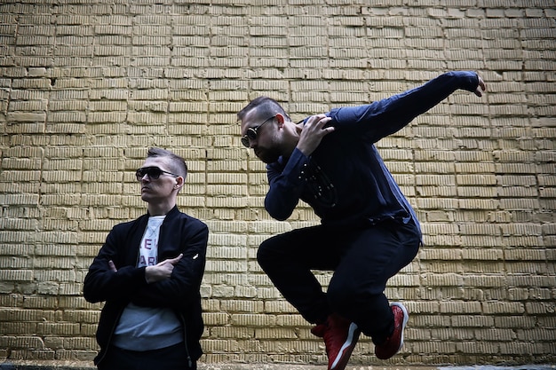 Two men in sunglasses against a brick wall background