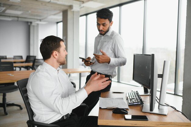 Two men traders sitting at desk at office together monitoring stocks data candle charts on screen analyzing price flow smiling cheerful having profit teamwork concept