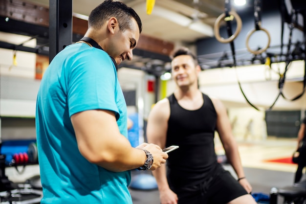 Photo two men training in gym looking at mobile phone