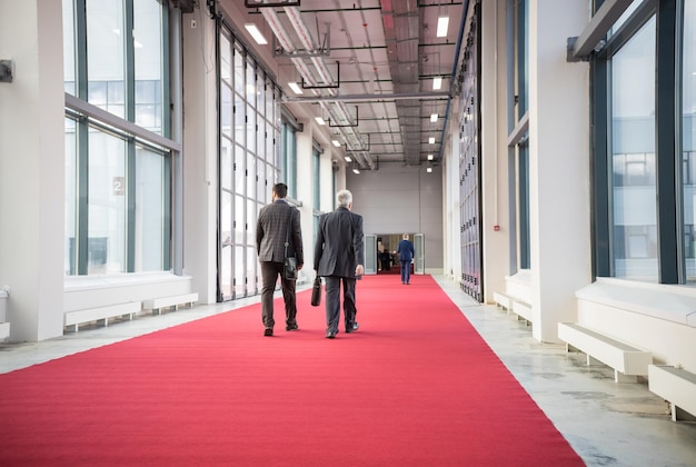 Two men walking on a red carpet towards a conference hall