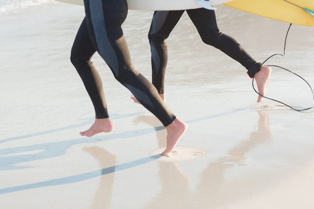 Two men in wetsuits with a surfboard on a sunny day