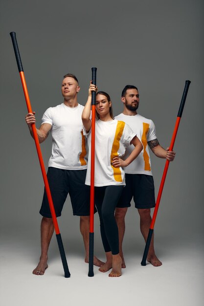 Photo two men and woman aikido fighters with wooden fight stick posing in studio fight demonstration