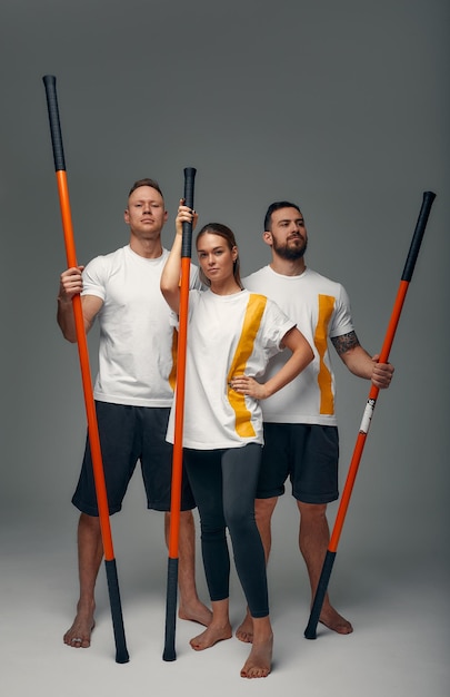 Two men and woman aikido fighters with wooden fight stick\
posing in studio fight demonstration