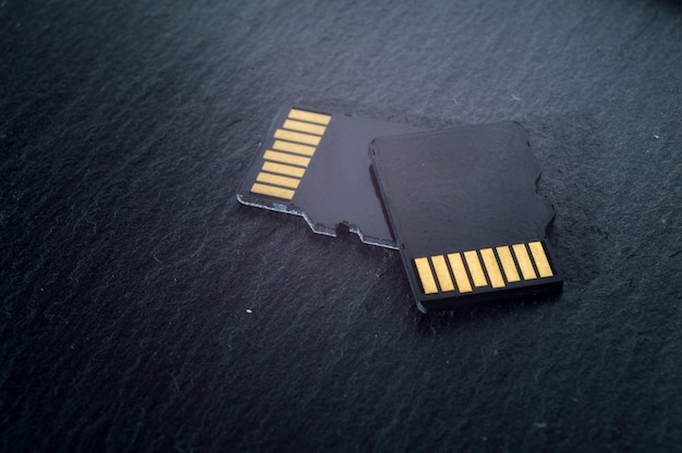 Two micro sd cards lie on top of each other on a dark textured background, with golden contacts at the top. close-up.