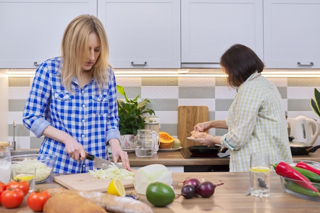 Two middle aged women cooking together at home in kitchen