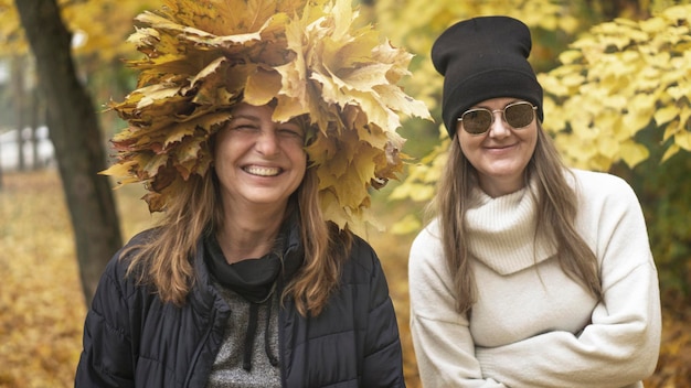 Two middle-aged women, friends are walking in the autumn park and laughing. Atmospheric brown toning, cinema effect. Selective focus. The concept of relationships between women.