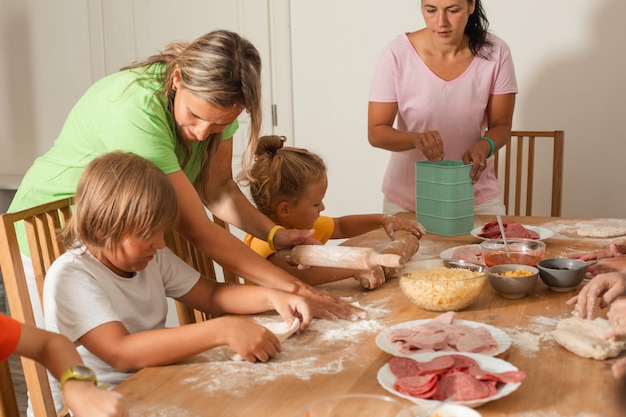 Two middleaged women with little children are making pizza